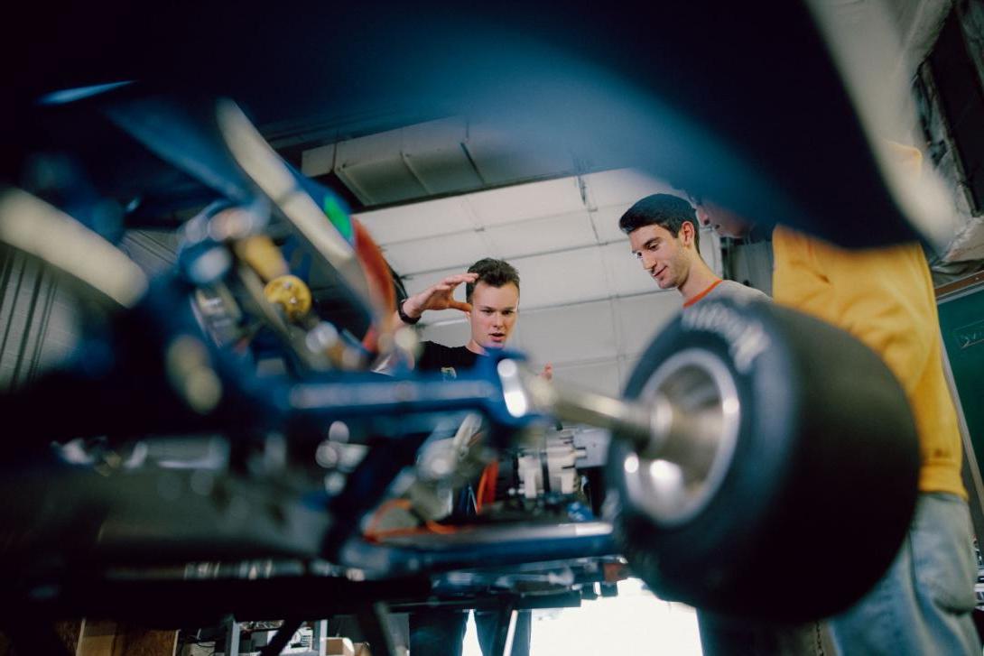 A group of Kettering electrical aengineering students stand over an electric vehicle and gesture toward it